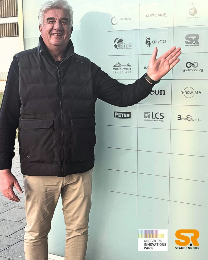André Begg vor der Partnertafel im Augsburg Innovationspark mit dem Staudenrohr-Logo